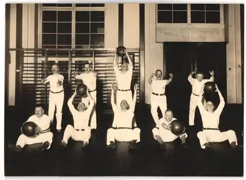 Fotografie unbekannter Fotograf und Ort, zehn Herren im Sportdress bei Turnübungen mit Medizinbällen, 1928