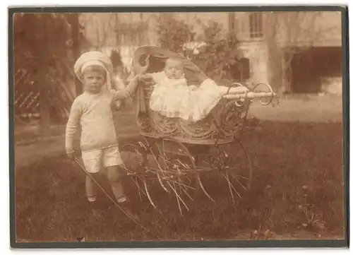 Fotografie unbekannter Fotograf und Ort, junger Knabe mit Geschwisterchen im Kinderwagen posieren im Garten