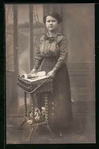 Foto-AK Junge Frau im Kleid blättert in einer Zeitschrift vor Studiokulisse