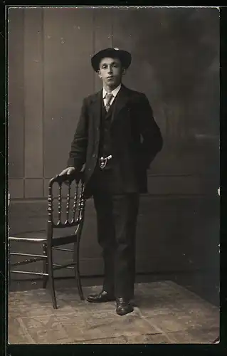 Foto-AK Jüngling im Dreiteiler, an einem Stuhl stehend, vor Studiokulisse