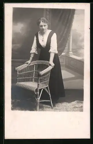 Foto-AK Junge Frau, auf einen Korbsessel gestützt, vor Studiokulisse