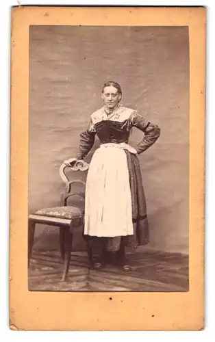 Fotografie unbekannter Fotograf und Ort, Dame im österreichischen Trachtenkleid posiert stehend am Stuhl