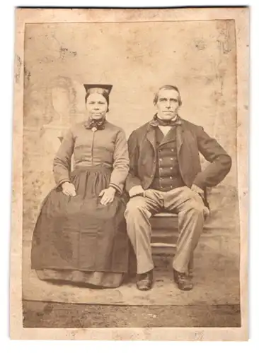 Fotografie unbekannter Fotograf und Ort, älteres Paar in Trachtenkleidern posieren sitzend im Atelier