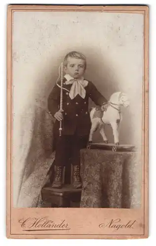 Fotografie C. Holländer, Nagold, junger Knabe im Anzug mit Gerte und Spielzeug Pferd im Atelier