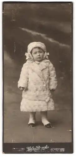 Fotografie Gebr. Strauss, Heidelberg, Portrait kleines Mädchen im weissen Wintermantel mit Wintermütze