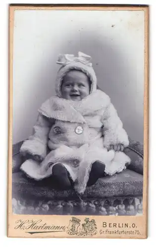 Fotografie Hartmann, Berlin, niedliches Kleinkind im weissen Winterpelz mit Haube und Schleife