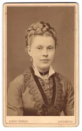Fotografie Bernh. Francke, Spremberg, junge Dame im bestickten Kleid mit geflochtenen Haaren und Ohrringen, Brosche