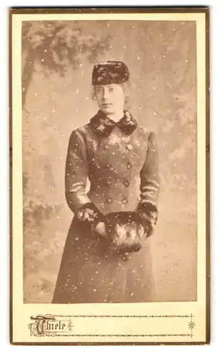 Fotografie Hugo Thiele, Frankfurt a. Main, Portrait junge Dame im Wintermantel mit Muff und Mütze, Schnee im Atelier