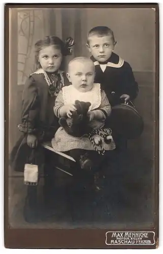 Fotografie Max Mennicke, Raschau i. Erzg., drei Kleinkinder in Kleidern und Matrosenanzug mit Teddybär im Arm