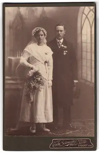Fotografie Centa Schneider, Endorf, Brautpaar im Hochzeitskleid und Mantel mit Orden Bayern Militär-Verdienstkreuz