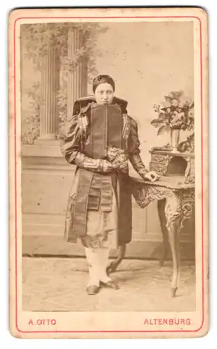 Fotografie A. Otto, Altenburg, junge Frau in Altenburger Tracht posiert stehend am Sekretär