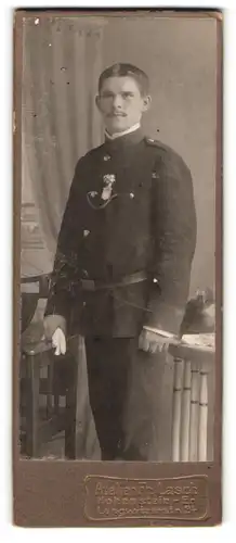 Fotografie Fr. Lasch, Hohenstein-Ernstthal, junger Feuerwehrmann in Uniform mit Anstecker und Helm auf dem Tisch