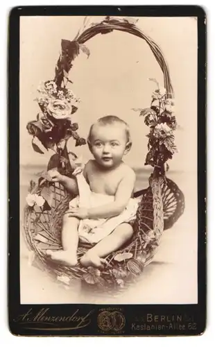 Fotografie A. Menzendorf, Berlin, Kleinkind im halb ausgezogenen Kleidchen posiert im Weidenkorb