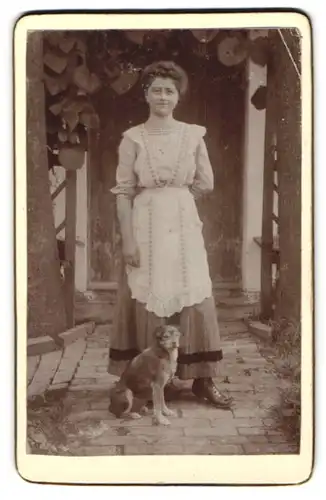 Fotografie unbekannter Fotograf und Ort, junge Frau im Hausfrauenkittel mit ihrem Hund zu Füssen