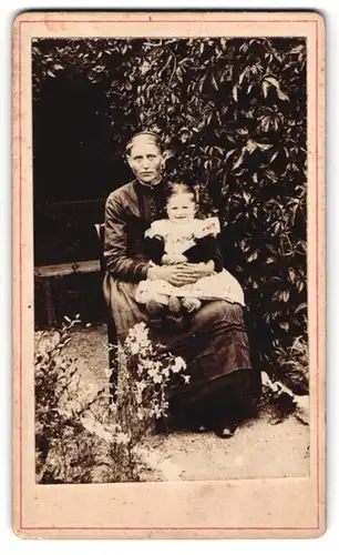 Fotografie unbekannter Fotograf und Ort, junge Frau mit ernstem Blick und Kleinkind auf dem Schoss