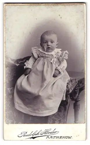 Fotografie Rudolph Hörder, Rathenow, Bahnhofstrasse, Goldiges Kleinkind mit Knopfaugen im übergrossen Kleidchen