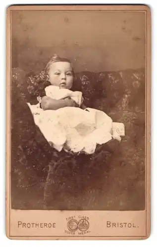 Fotografie Protheroe, Bristol, Wine Street 35 u. 36, Kleinkind im Spitzenkleid auf dem Sofa