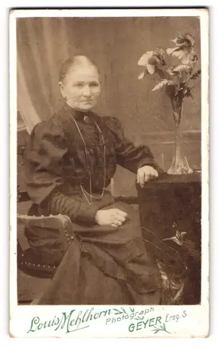 Fotografie Louis Mehlhorn, Geyer i. Ezg., Ältere Dame im plissierten Kleid neben Blumen