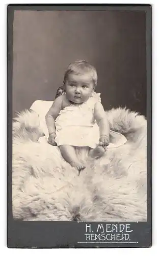 Fotografie H. Mende, Remscheid, Süsses Kleinkind im Hemd sitzt auf Fell