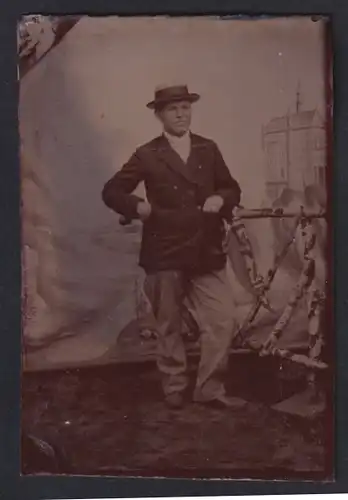 Fotografie Ferrotypie Herr im Anzug mit Hut posiert vor einer bemalten Leinwand