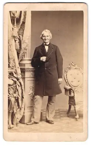 Fotografie Gustav Schultze, Naumburg a. S., älterer Herr im Anzug mit Fliege posiert grinsend im Atelier