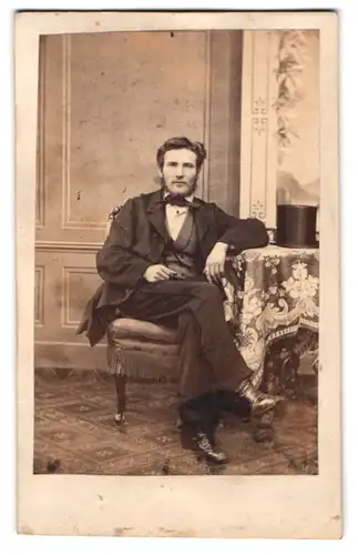 Fotografie E. May, Halle a. S., junger Mann im Anzug mit Vollbart und Zylinder auf dem Tisch