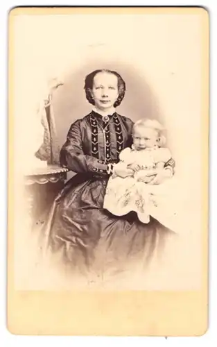 Fotografie Otto Wigand, Zeitz, Portrait Mutter im bestickten Kleid mit ihrer Tochter auf dem Schoss
