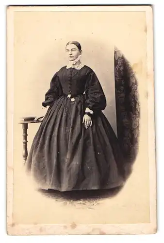 Fotografie unbekannter Fotograf und Ort, junge Frau Hannah im dunklen Reifrockkleid mit Brille, 1864