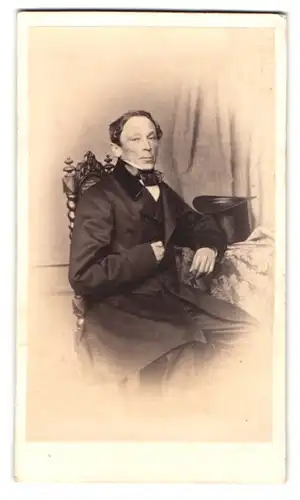 Fotografie L. Hohbach, Constanz, Portrait älterer Herr im Anzug mit Zylinder auf dem Tisch