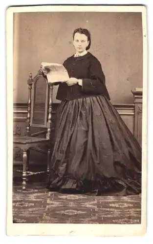 Fotografie unbekannter Fotograf und Ort, Portrait junge Frau im dunklen Kleid mit Jacke liest eine Zeitung