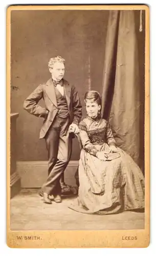 Fotografie W. Smith, Leeds, junges englisches Paar im Anzug mit Fliege und im karierten Kleid mit Halskette