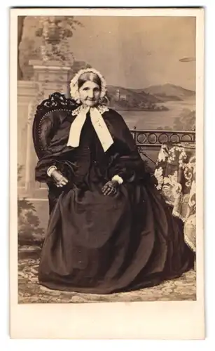 Fotografie unbekannter Fotograf und Ort, älter Dame im schwarzen Kleid mit heller Haube und Lederhandschuhen