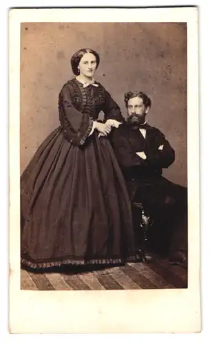Fotografie F. Halm, Constanz, Paar im schwarzen Reifrockkleid und Herr im Anzug mit Vollbart