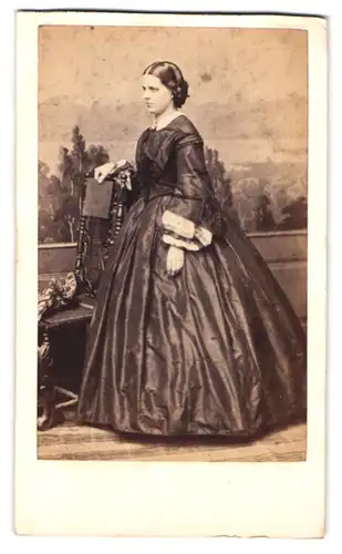 Fotografie F. Halm, Constanz, Portrait junge Frau im seidenen Kleid vor einer Studiokulisse