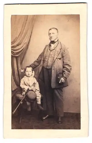 Fotografie unbekannter Fotograf und Ort, Grossvater im Anzug mit Engelson samt Melone und Flanierstock im Atelier