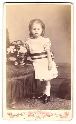 Fotografie Doidge & Co., Plymouth, Union Street, Mürrisch schauendes kleines Mädel mit Blumenkorb