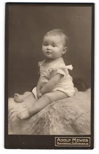 Fotografie Adolf Mewes, Rathenow, Schützenstr. 28, Portrait niedliches Baby im Kleidchen auf einem Fell sitzend