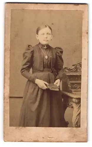 Fotografie unbekannter Fotograf und Ort, Portrait von Emma im gerüschten Kleid mit Medaillon und Buch