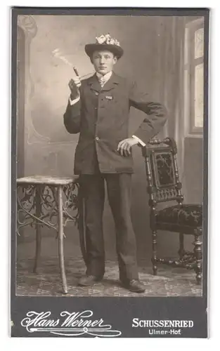 Fotografie Hans Werner, Schussenried, junger Mann mit Nummer am Anzug zur Musterung raucht Zigarre aus einer Pfeife