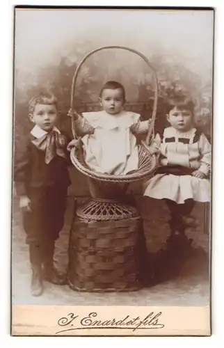 Fotografie J. Enard et fils, Delemont, drei niedliche Kleinkinder in Kleidern mit Geschwisterchen im Weidenkorb