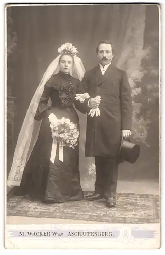 Fotografie M. Wacker Wwe., Aschaffenburg, Hochzeitspaar im schwarzen Kleid mit weissem Schleier und im Anzug mit Zylinder