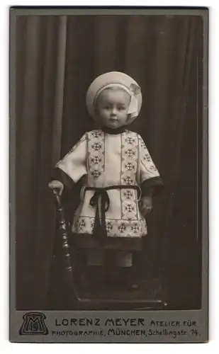 Fotografie Lorenz Meyer, München, niedliches Kleinkind im schicken Kleidchen mit Sommerhut steht auf einem Stuhl
