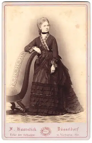 Fotografie F. Haarstick, Düsseldorf, junge blonde Dame im schwarzen Kleid mit gerafften Saum