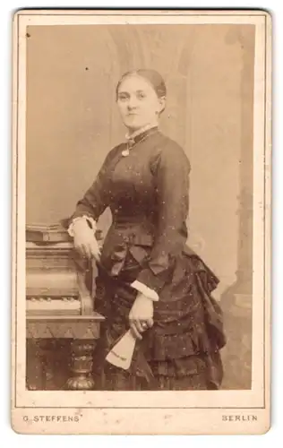 Fotografie G. Steffens, Berlin, Potsdamer-Str. 116a, Dame im Tournürenkleid mit Fächer am Piano, Ida