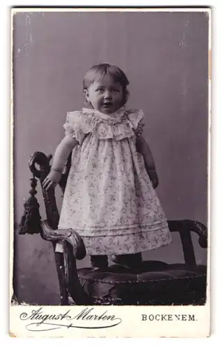 Fotografie August Marten, Bockenem, Kleinkind im gerüschten Kleid auf Stuhl stehend