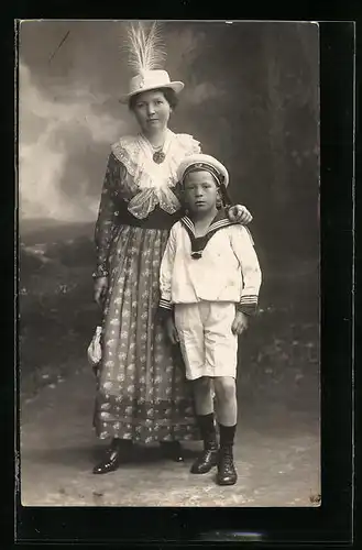Foto-AK Mutter mit Federhut neben ihrem Sohn im Matrosenanzug in Studiokulisse