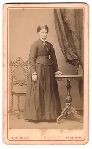 Fotografie W. Grigoleit, Rathenow, Portrait elegant gekleidete Dame steht an einem Tisch