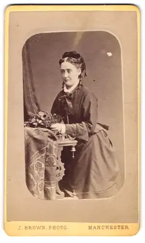 Fotografie J. Brown, Manchester, 41 Oxford Street, Portrait bildschöne junge Frau mit Blumenkorb am Tisch sitzend