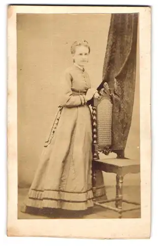 Fotografie unbekannter Fotograf und Ort, Portrait blonde junge Frau im Kleid an einem Stuhl stehend