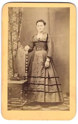 Fotografie unbekannter Fotograf und Ort, bildschönes Fräulein im prachtvollen Kleid am Stuhl stehend